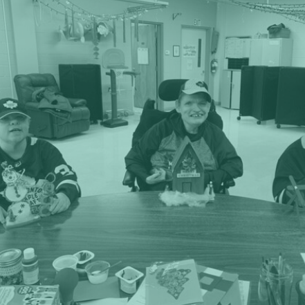 Three individuals participating in arts and crafts activities at a table.