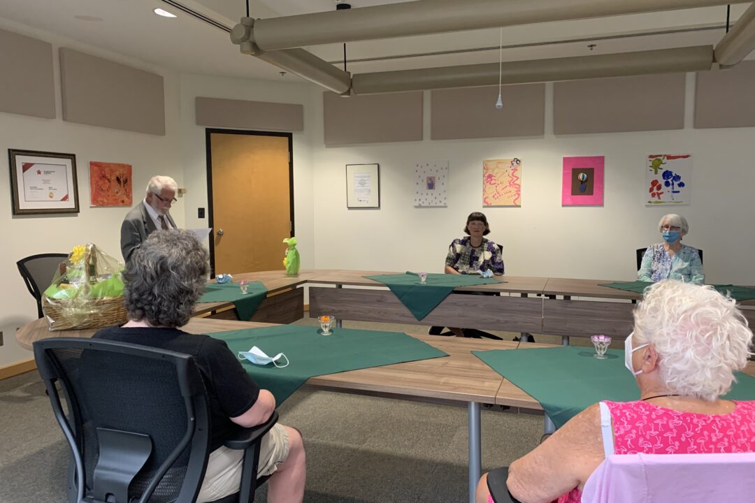 Group of individuals sitting around tables in a meeting room with artwork on the walls.