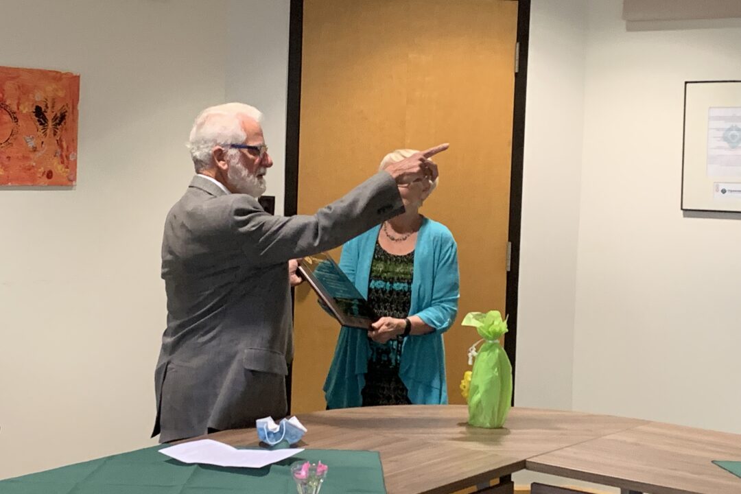 An elderly man presenting a certificate to a woman during a formal event indoors.