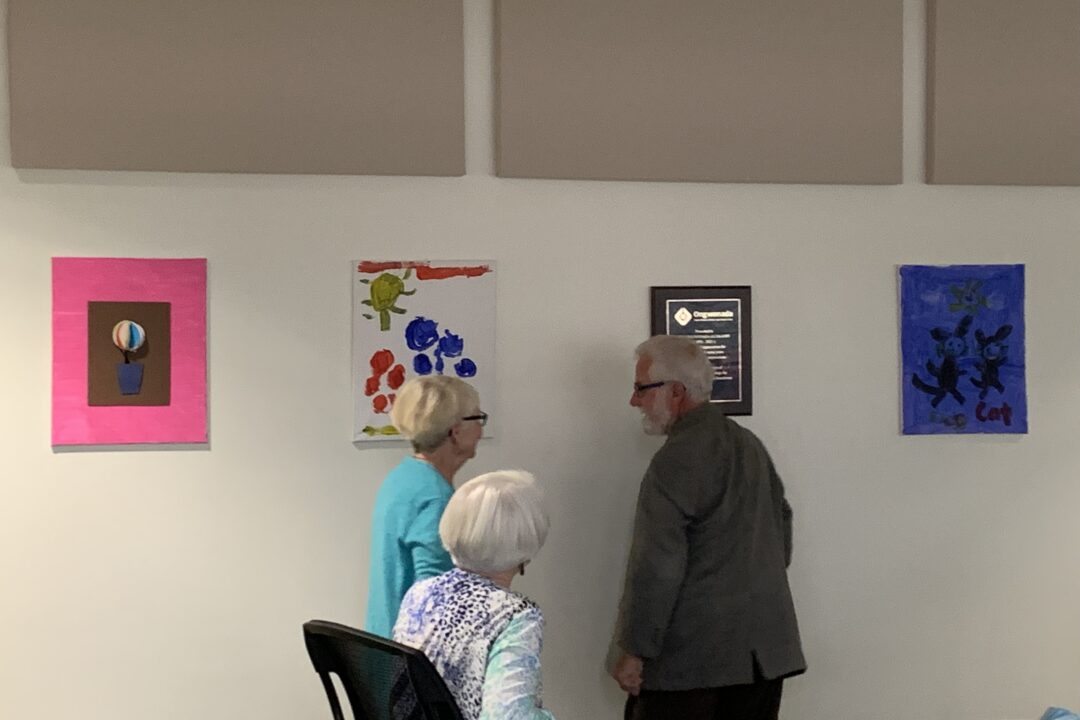Two individuals standing and conversing in a room with colorful artwork on the wall.