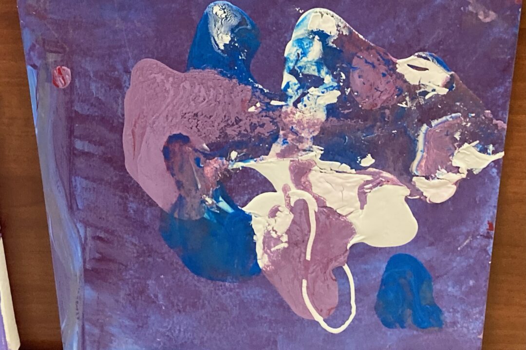 Abstract painting with blue and purple hues and white accents displayed on a brown surface.
