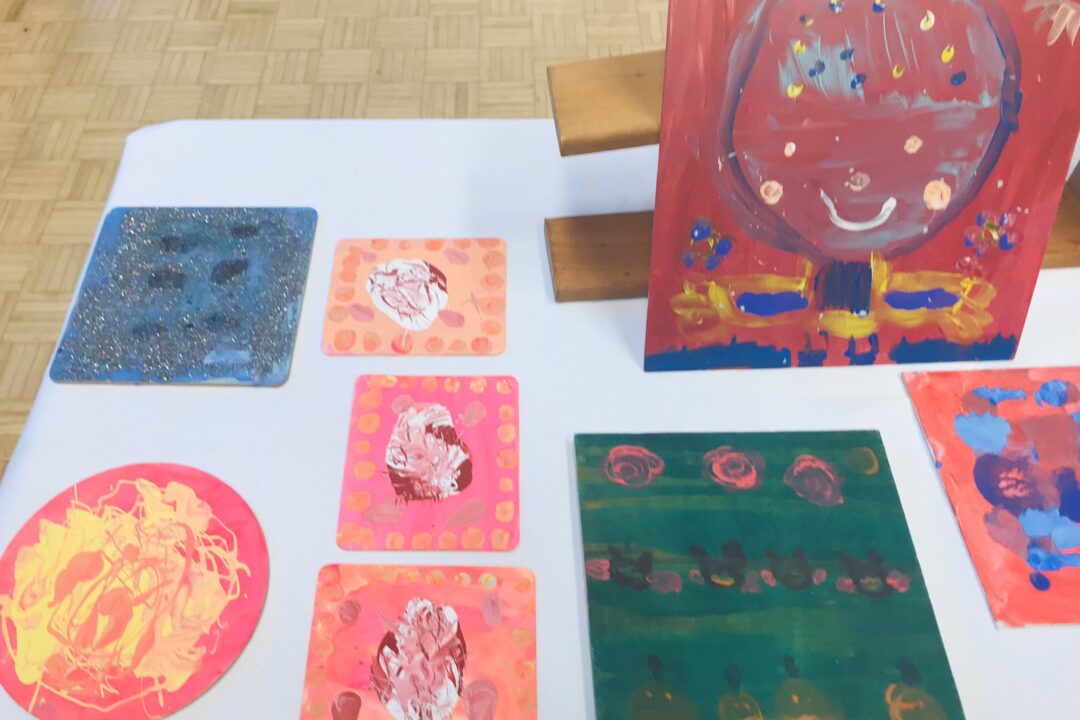 Children's colorful artwork displayed on the floor and an easel in a classroom setting.