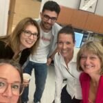 A group of five adults smiling for a selfie in a classroom setting.