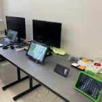 An office desk with multiple electronic devices, including computers, monitors, and a tablet.