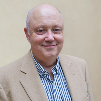 David A smiling bald man in a beige jacket and striped shirt against a neutral background.