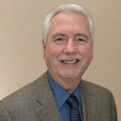 Smiling elderly man with white hair wearing a jacket and tie.